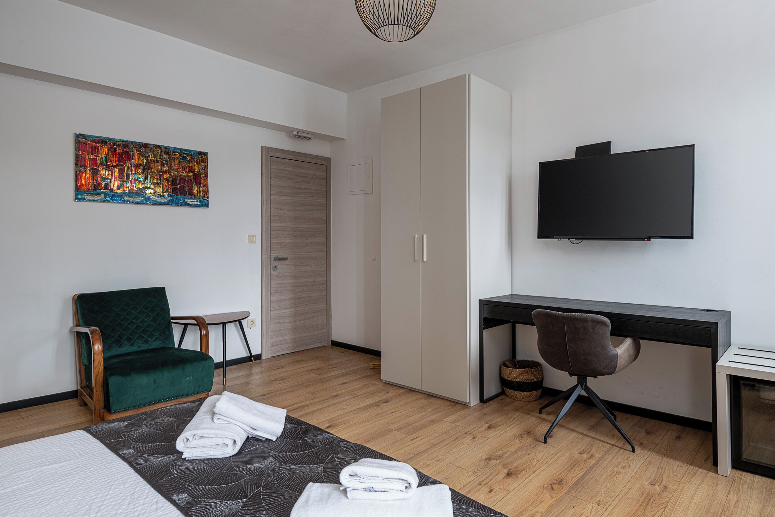 Una habitación de hotel moderna con una cama, un escritorio, una silla, un televisor y un cuadro en la pared.
