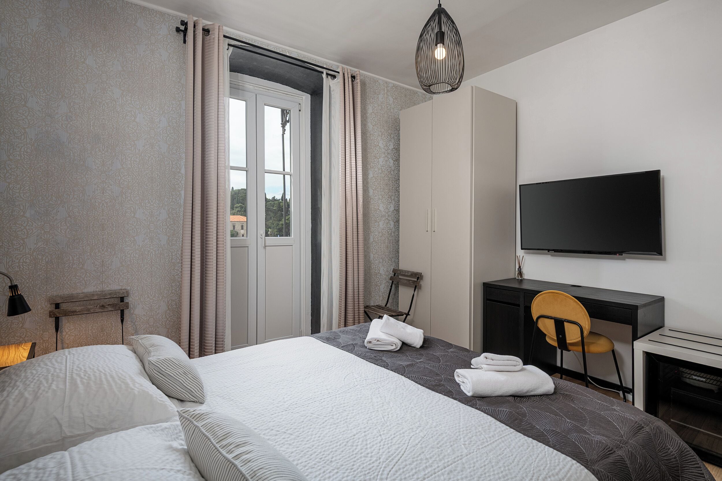 A hotel room with a bed, a desk, a chair, a television, and a view through a door.