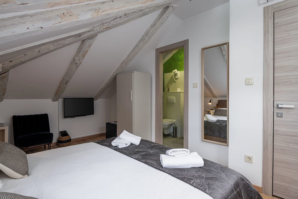 Un dormitorio con cama, televisor de pantalla plana, armario y baño visible a través de una puerta abierta.