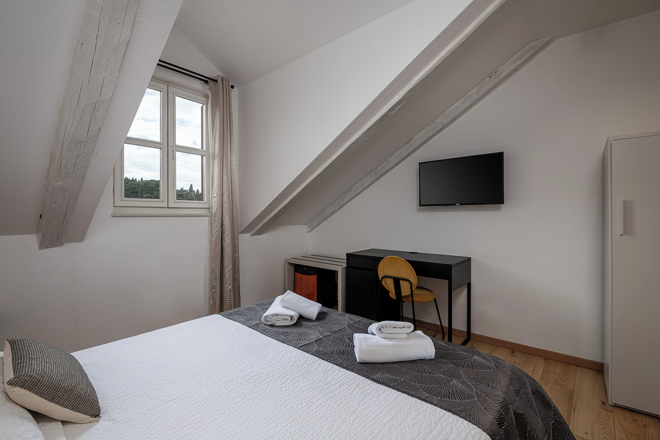 Een slaapkamer met een bed, een bureau, een stoel, een televisie en een raam.