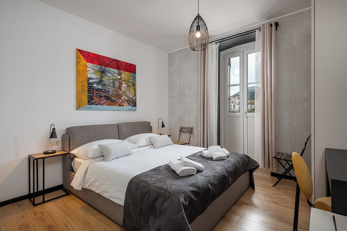 Un dormitorio moderno con una cama grande, un escritorio, una silla y una ventana con cortinas.