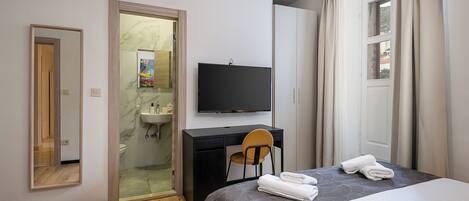 A modern hotel room with a bed, a desk, a chair, a TV, a bathroom, and a wardrobe.