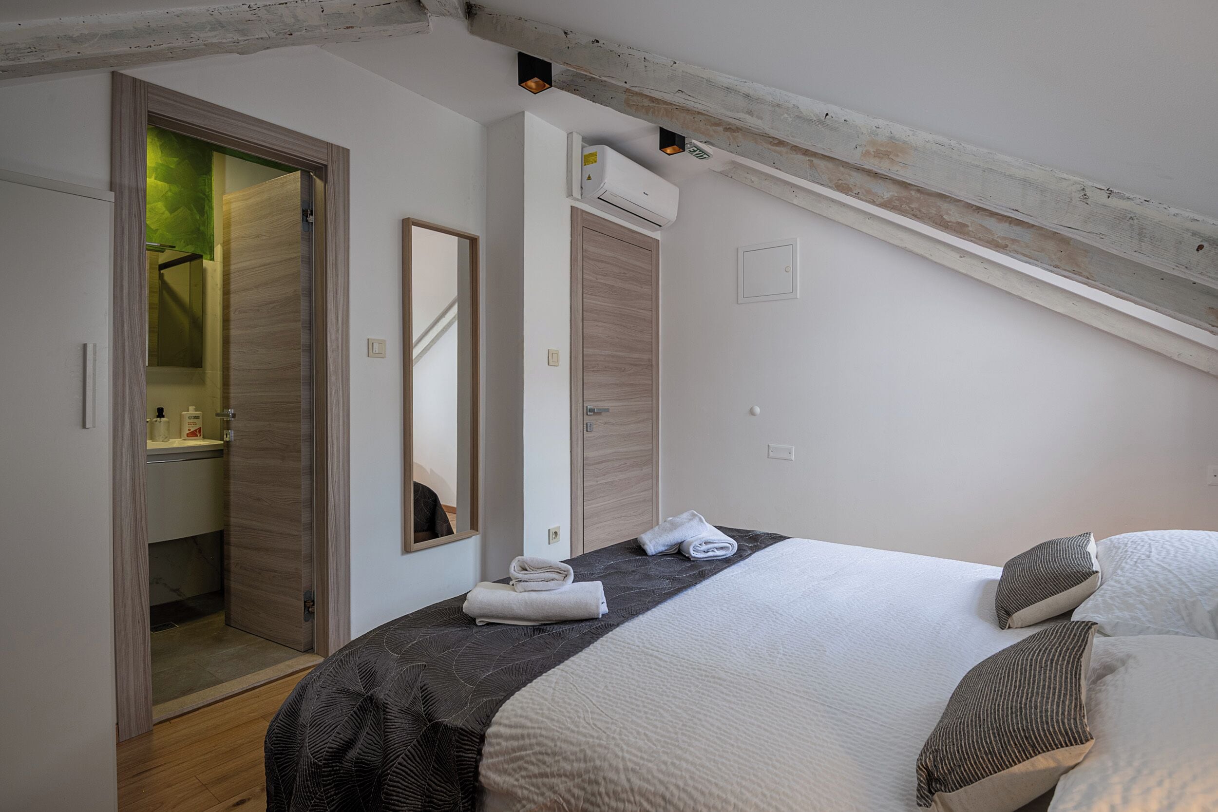Une chambre à coucher comprenant un lit, un miroir, un appareil de climatisation et une porte donnant accès à une salle de bain.