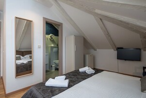 Quarto com cama grande, espelho, guarda-roupa, televisão e banheiro visível por uma porta aberta.