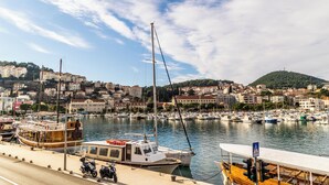 Uma marina com barcos atracados, uma faixa de pedestres e vista para o horizonte urbano com edifícios e uma colina ao fundo.
