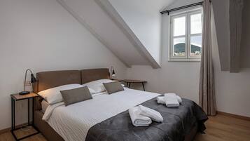 A bedroom with a bed, bedside tables, a window with curtains, and a view of a hill.