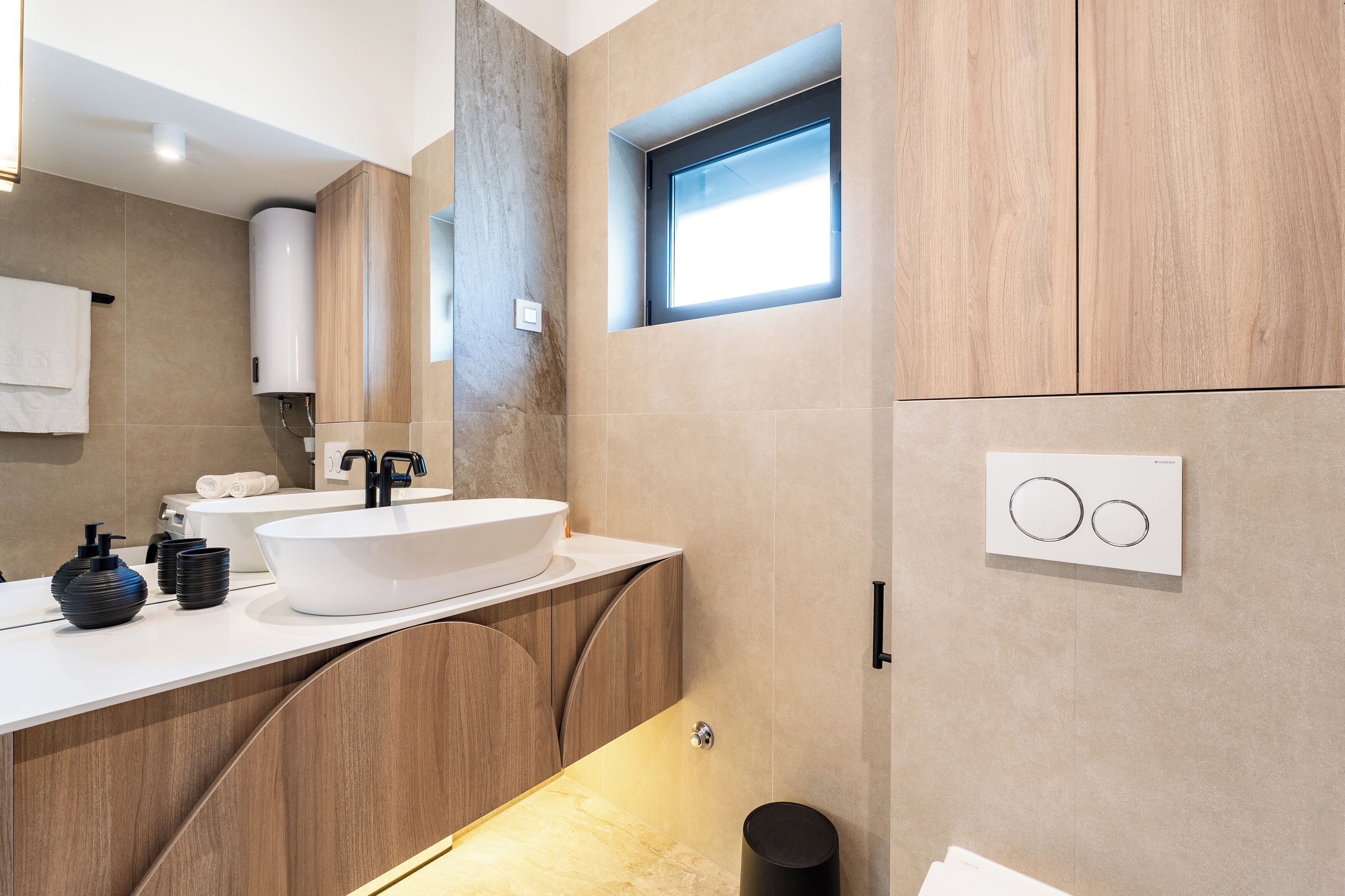 A modern bathroom with a large sink, wooden cabinetry, a window, and a towel rack.