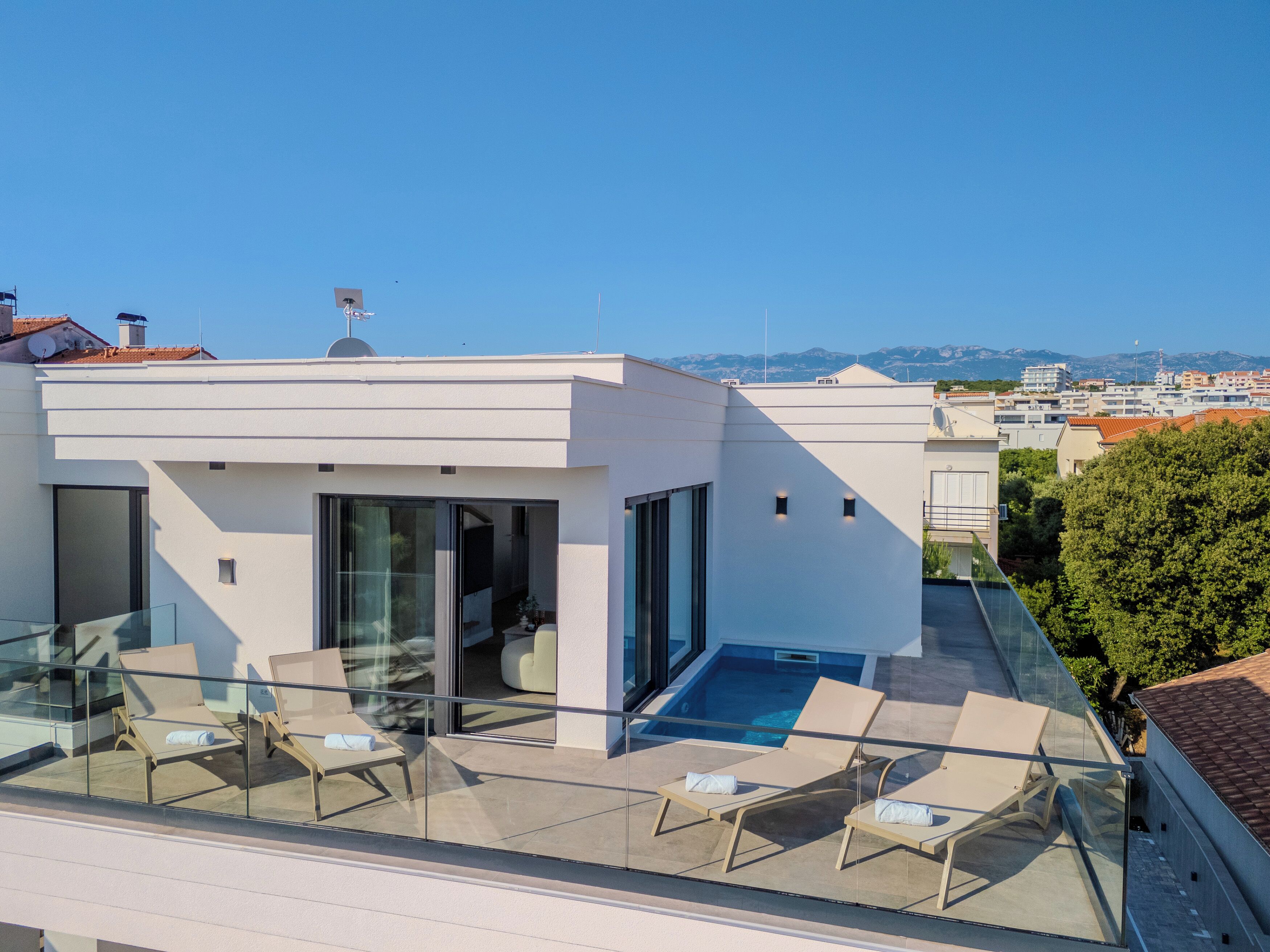 Ein modernes Gebäude mit einem Glasbalkon, Liegestühlen und einem Pool.