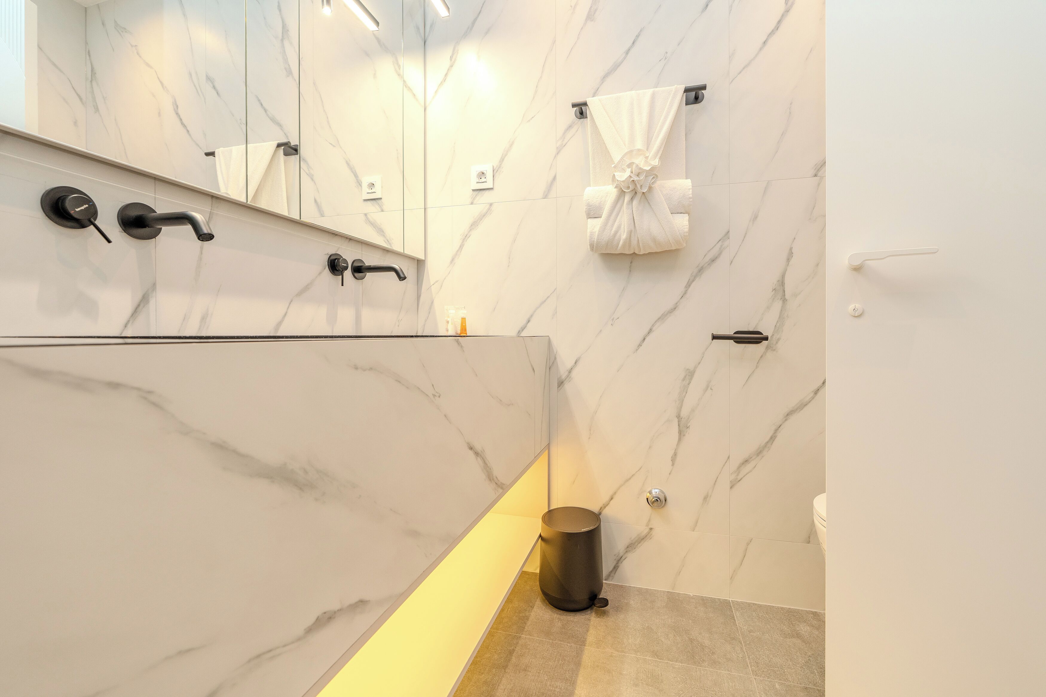 Une salle de bain moderne avec des murs en marbre, une douche en verre et des toilettes.