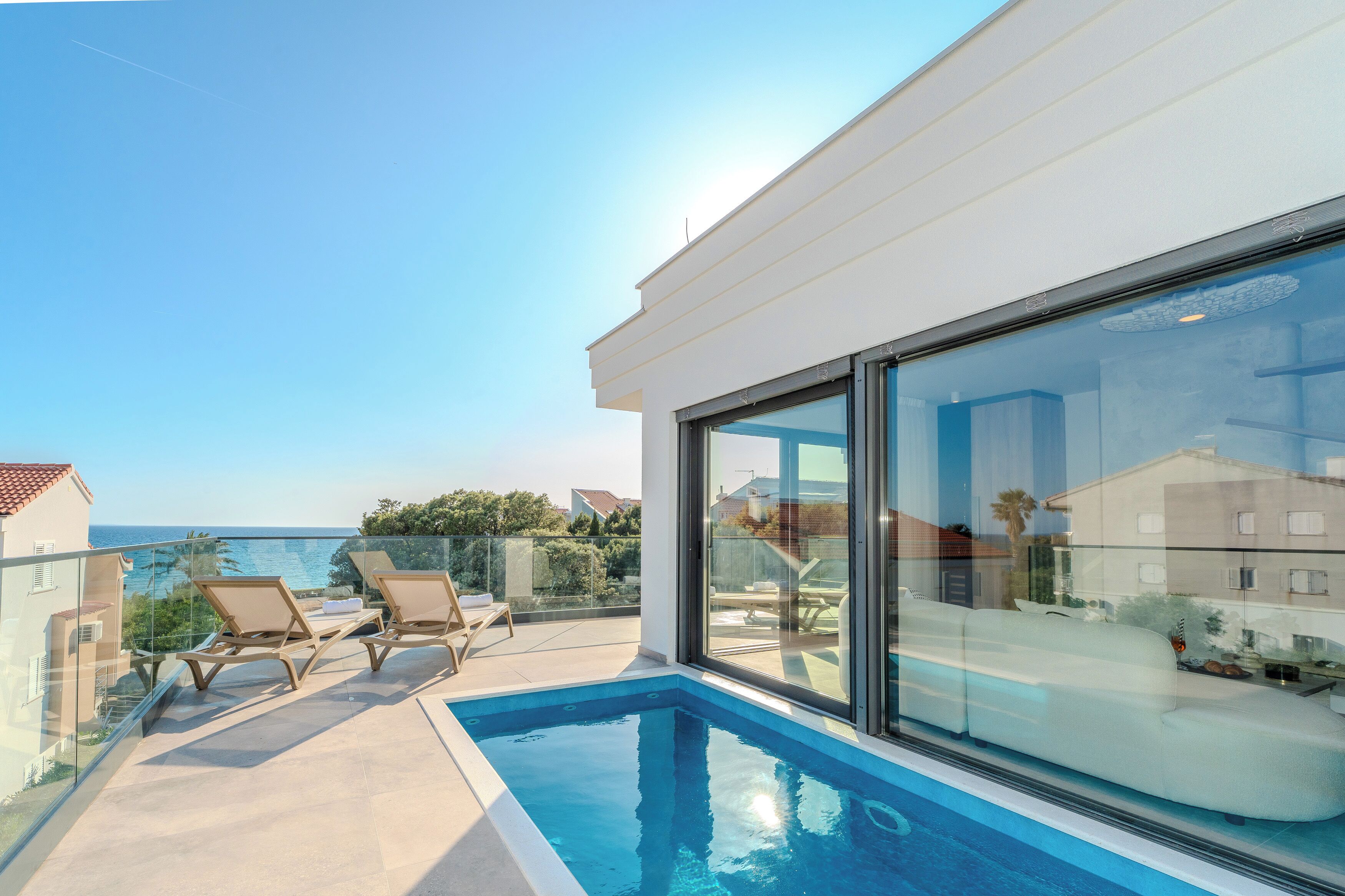 A modern balcony with a pool, lounge chairs, and a view of the sea.