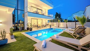A modern two-story house with a swimming pool, outdoor seating, and a well-maintained lawn.
