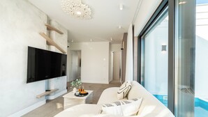 A modern living room with a flat-screen TV, a sofa with decorative pillows, a coffee table with a tray, and a large window offering a view.