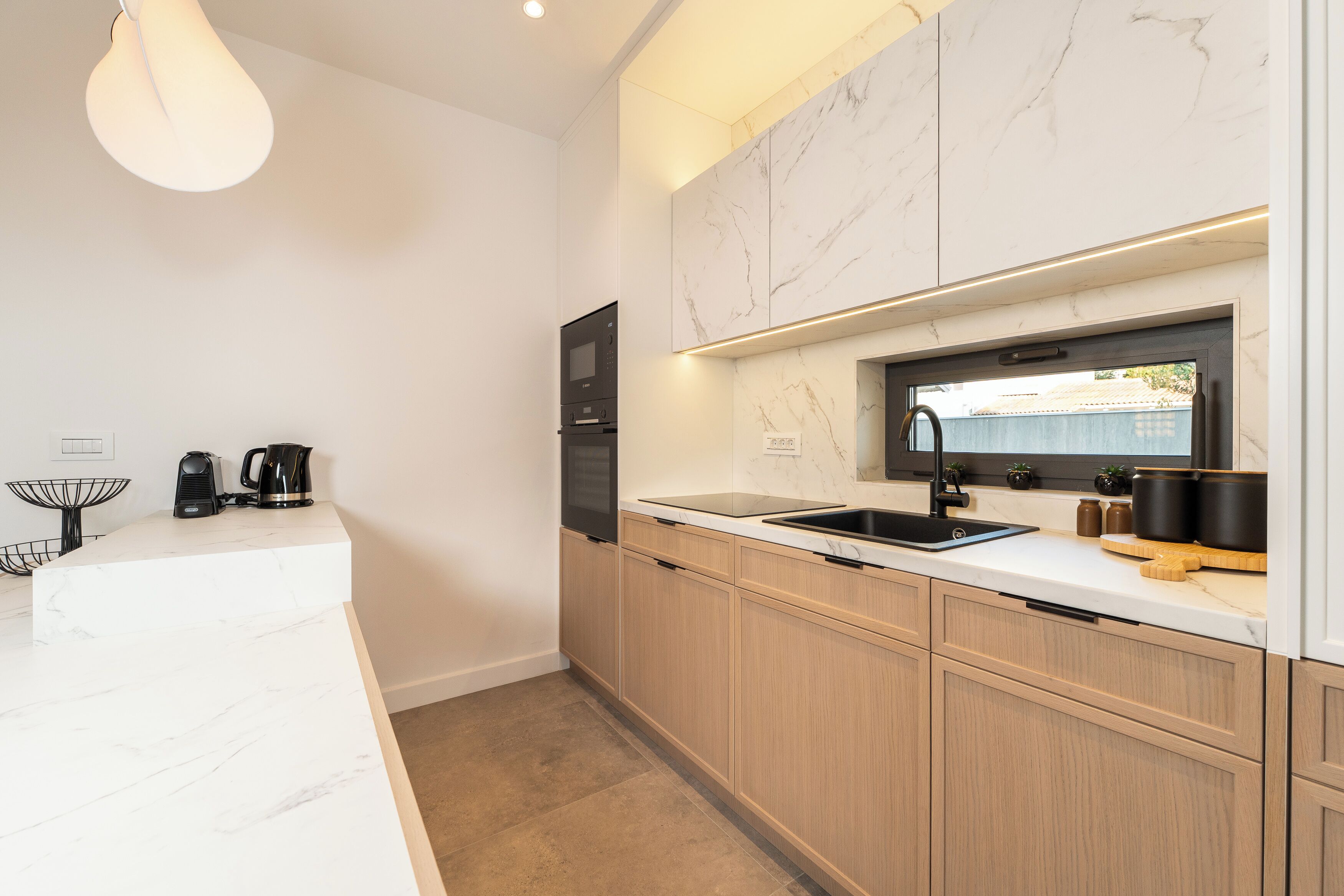 A modern kitchen with white marble countertops, wooden cabinets, and a built-in oven.
