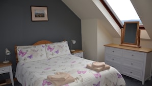 Un dormitorio con cama, mesitas de noche, cómoda, espejo y tragaluz.