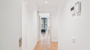 Un couloir avec un plancher en bois, des murs blancs et une porte sur le côté gauche. Deux appareils sont fixés au mur sur le côté droit.