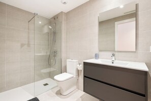 Un baño moderno con cabina de ducha de vidrio, inodoro y tocador con espejo.