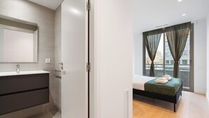 Une chambre à coucher moderne avec un lit, une fenêtre avec des rideaux et une salle de bain équipée d’un miroir et d’un lavabo.