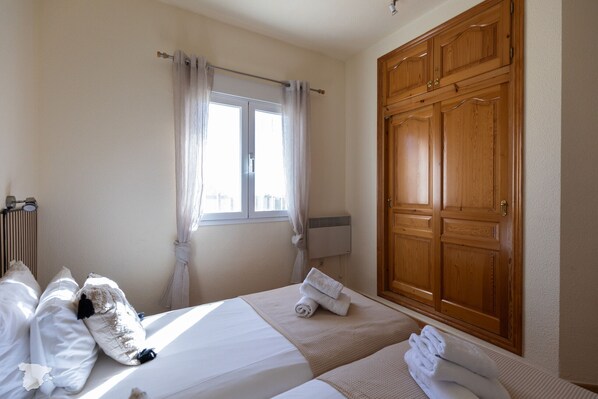 A hotel room with two beds, a large wooden wardrobe, a radiator, and a window with curtains.