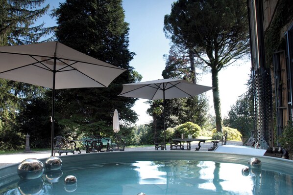 Relax by the pool surrounded by lush trees and shaded by two umbrellas.