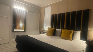 A hotel room with a large bed, a wardrobe, a mirror, and a bedside table.