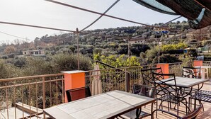 Terraza al aire libre con mesas y sillas, con vistas a una colina con edificios y árboles.