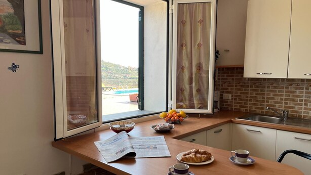 Una cocina con encimera de madera, ventana con cortinas, pileta y alacenas.
