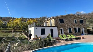 Un edificio de piedra con piscina, sillones reclinables verdes y un cielo azul despejado.