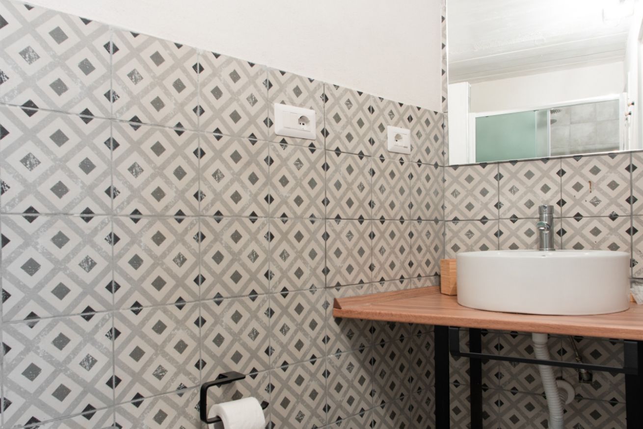 Un baño con baldosas estampadas, un lavabo blanco, una encimera de madera y un espejo sobre el lavabo.