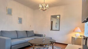 A modern living room with a grey sofa, a round coffee table, a chandelier, a mirror, and a lamp.