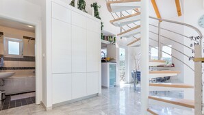 A modern kitchen with white cabinets, a built-in sink, and a spiral staircase with wooden steps. - Apartment Aqua-Juric (Crikvenica)