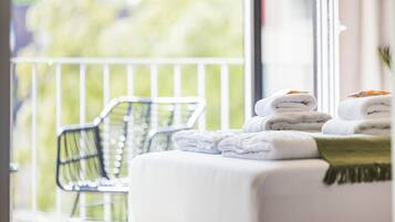 Relax on the balcony with a peaceful view of lush greenery, featuring a comfortable bed and a cozy throw blanket.