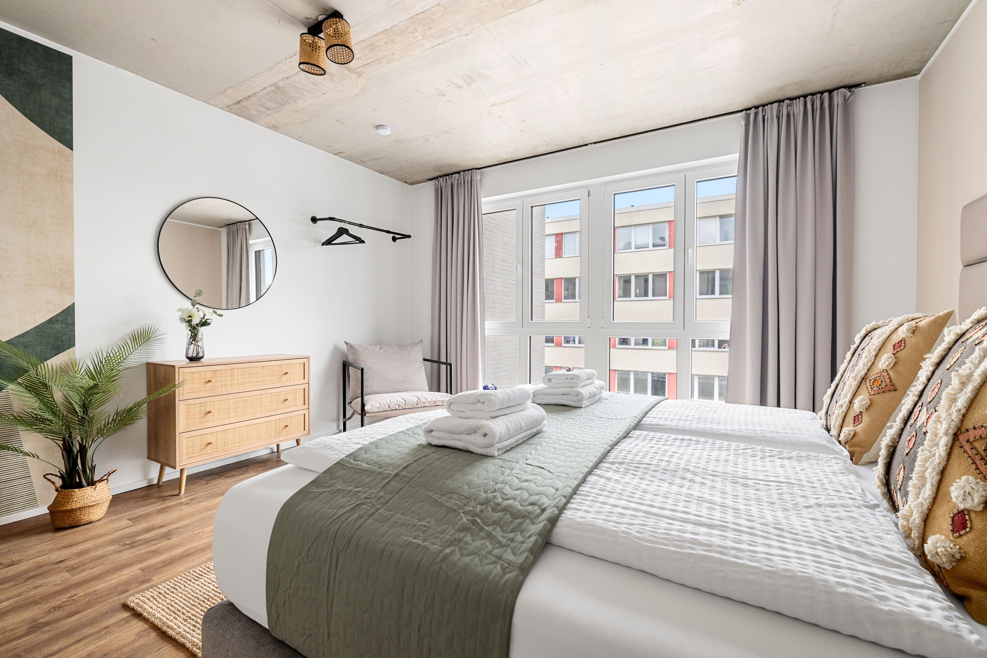 Een moderne hotelkamer met een groot bed, een houten dressoir, een spiegel en uitzicht op de stad.