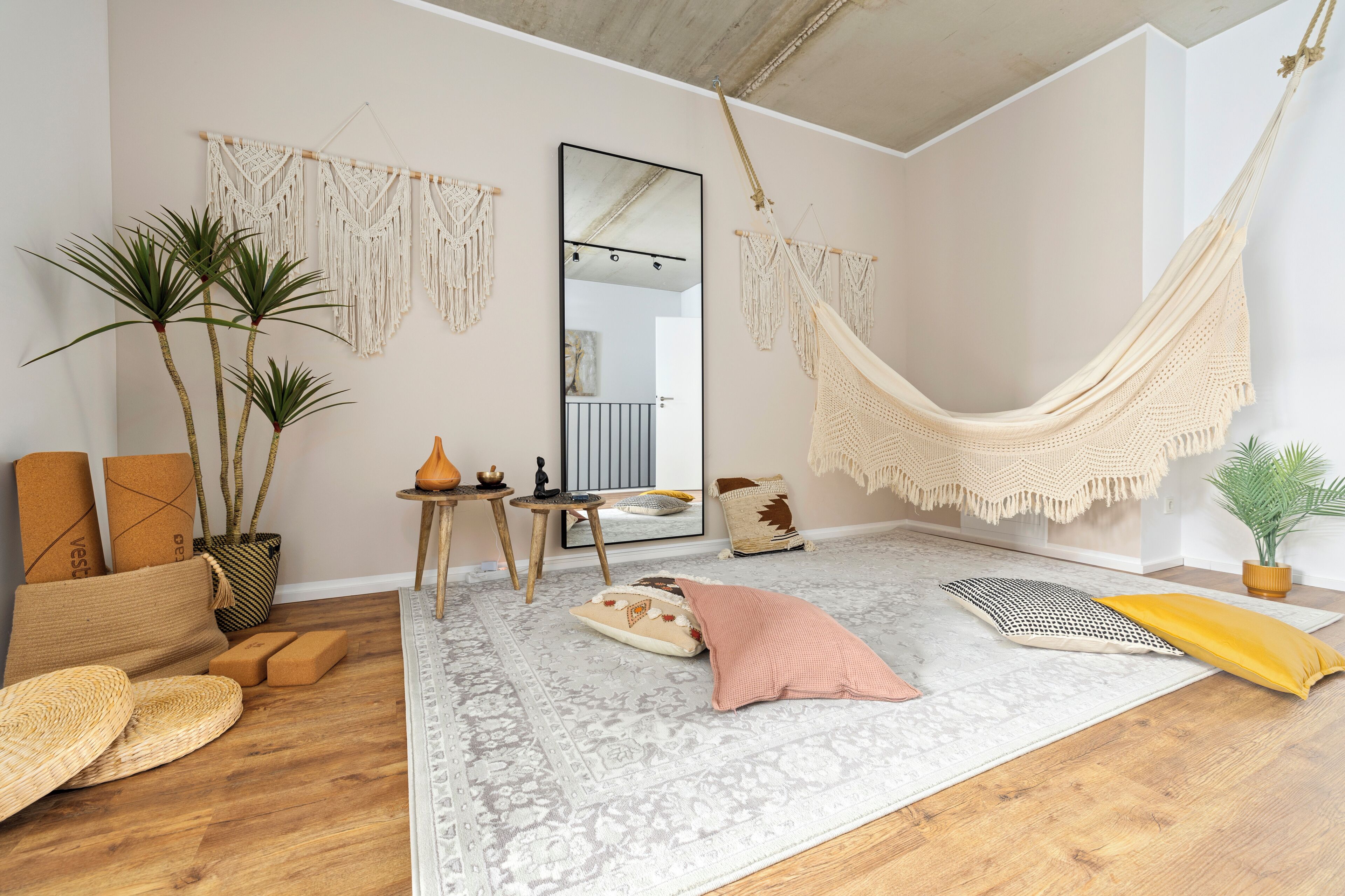 Ein Zimmer mit einer Hängematte, Wandbehängen aus Makramee, einem großen Spiegel und einem gemusterten Teppich.