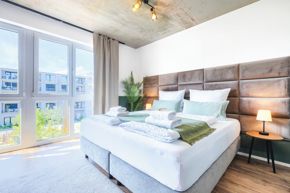 Um quarto moderno com uma cama grande, cabeceira, mesa de cabeceira e vista para o exterior.