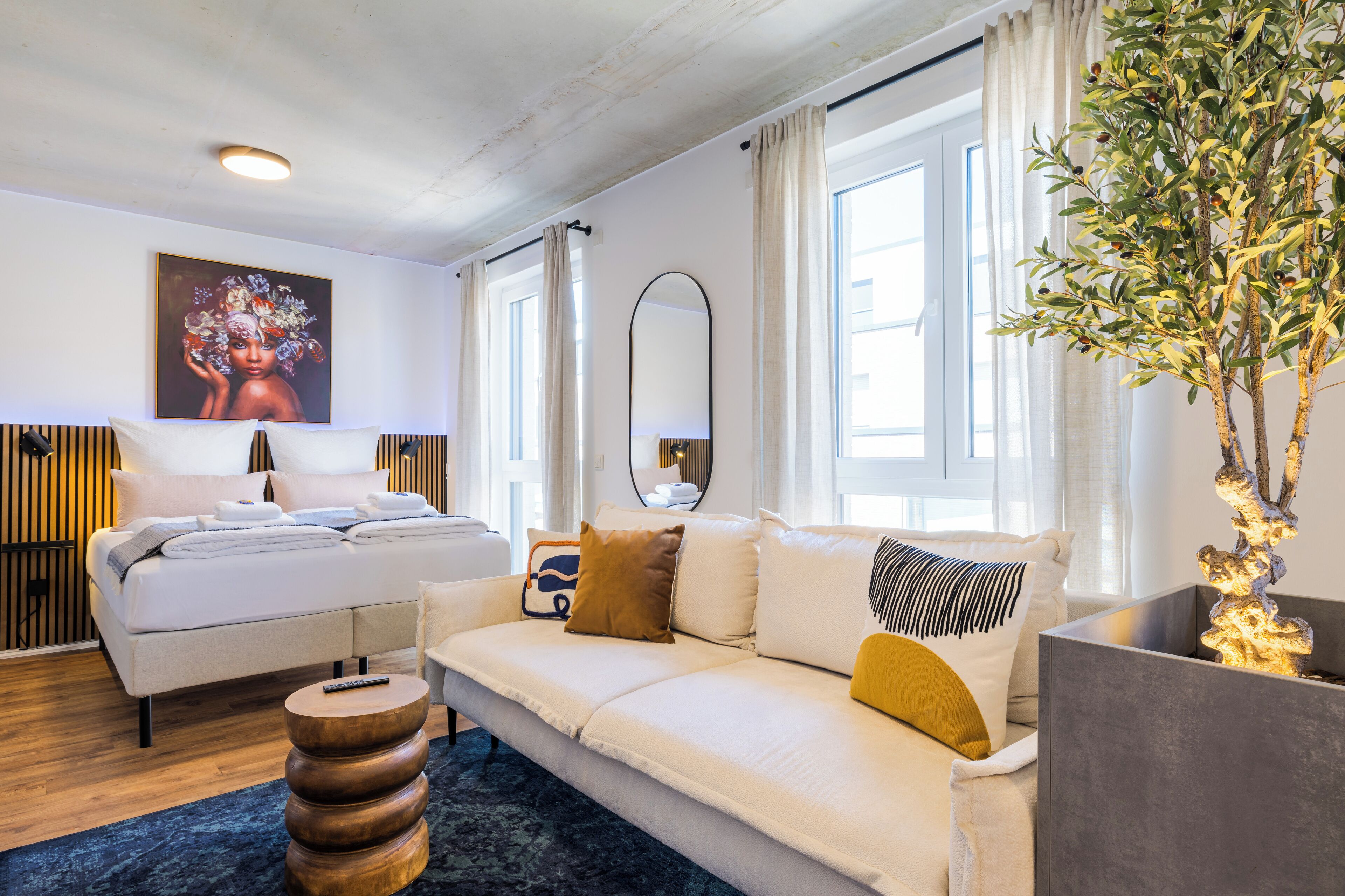 A modern hotel room with a bed, sofa, and a large mirror.