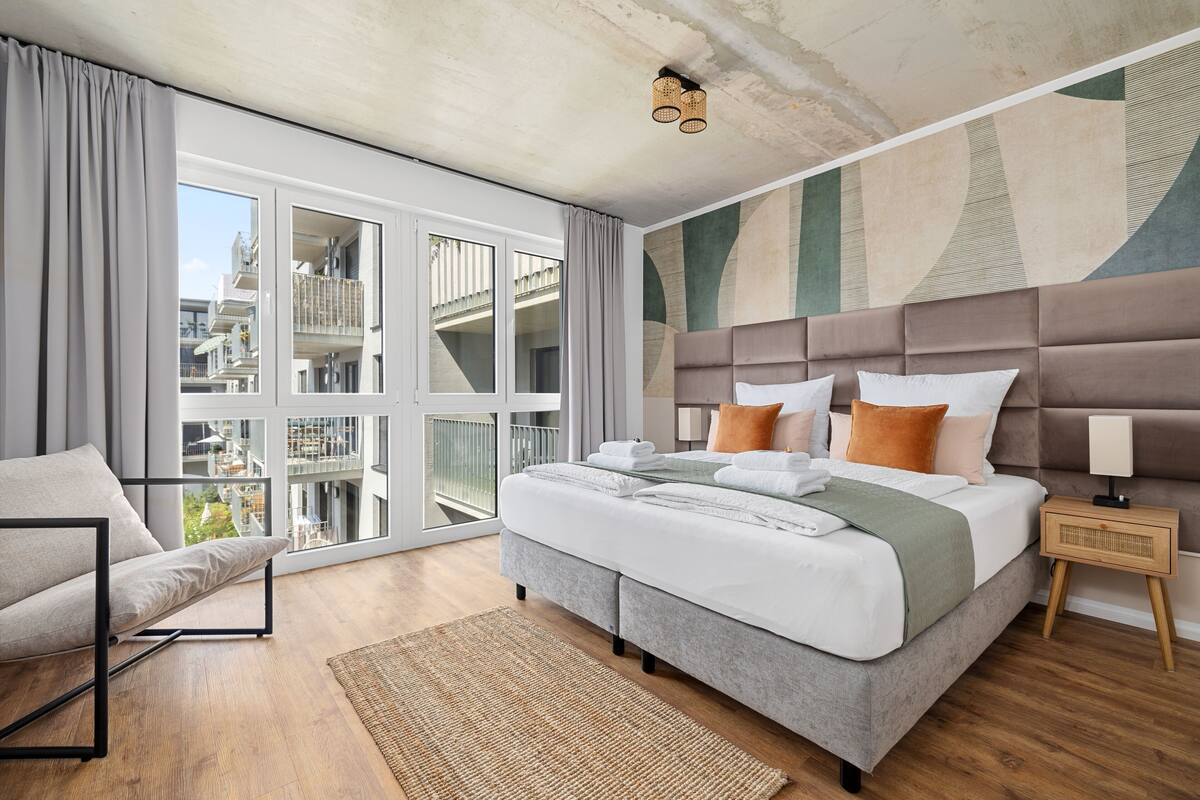 Quarto moderno com uma cama grande, vista de um edifício através de uma porta de vidro e varanda.