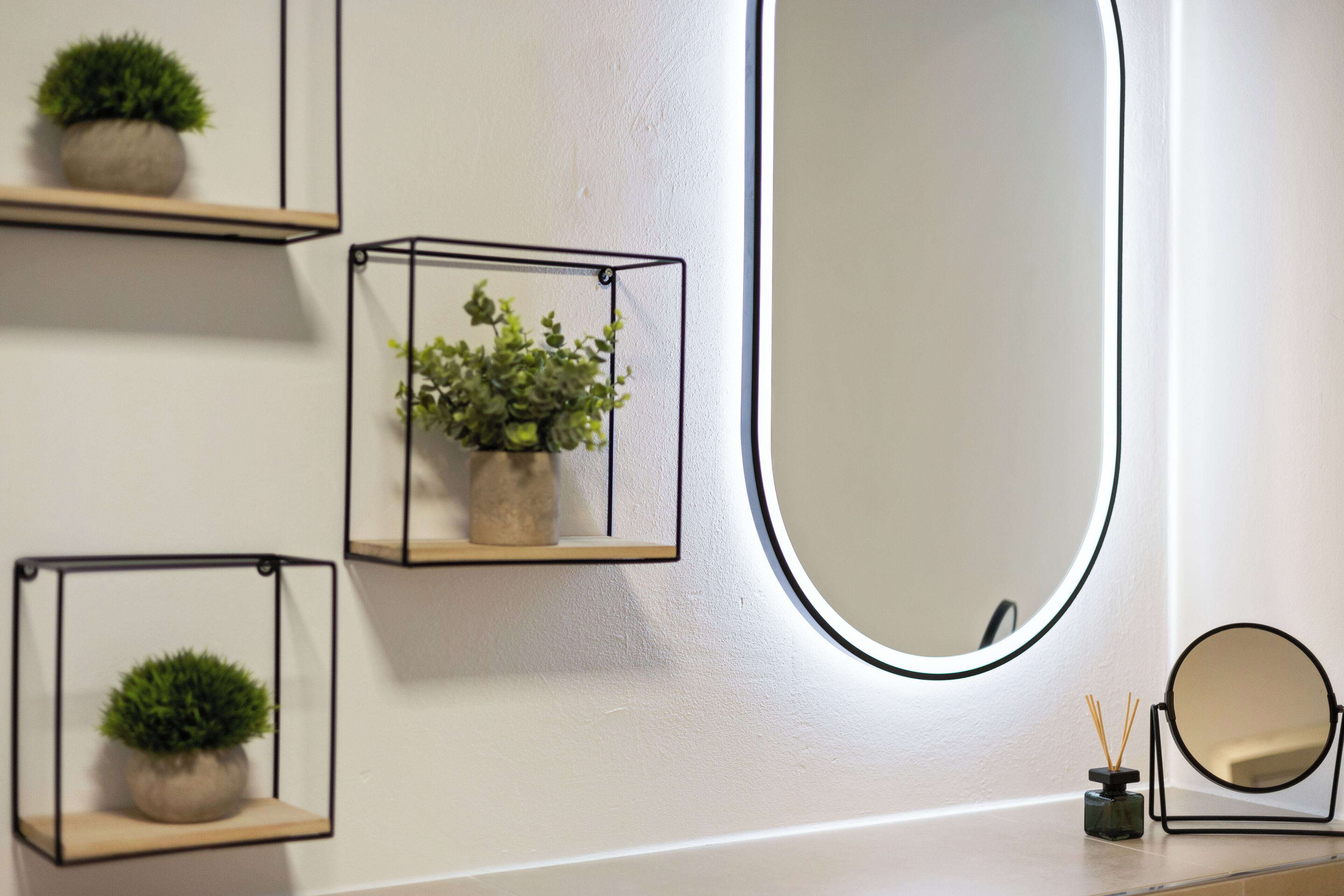 Une salle de bain avec trois étagères murales où sont disposées des plantes en pot, un grand miroir et un petit flacon de diffuseur de parfum à bâtonnets.