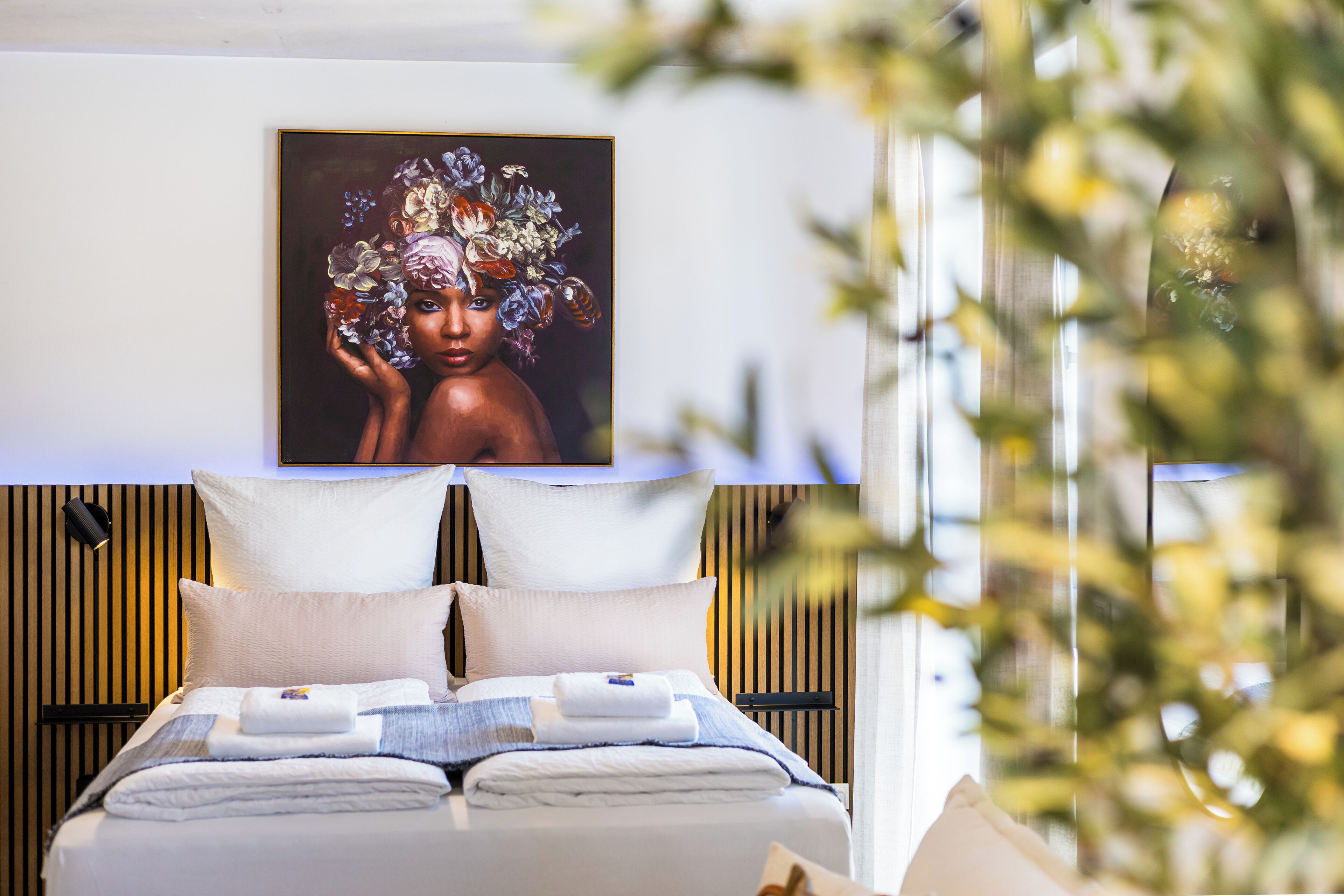 A modern hotel room with a large bed, a flat-screen TV mounted above it, and a wall-mounted light fixture.