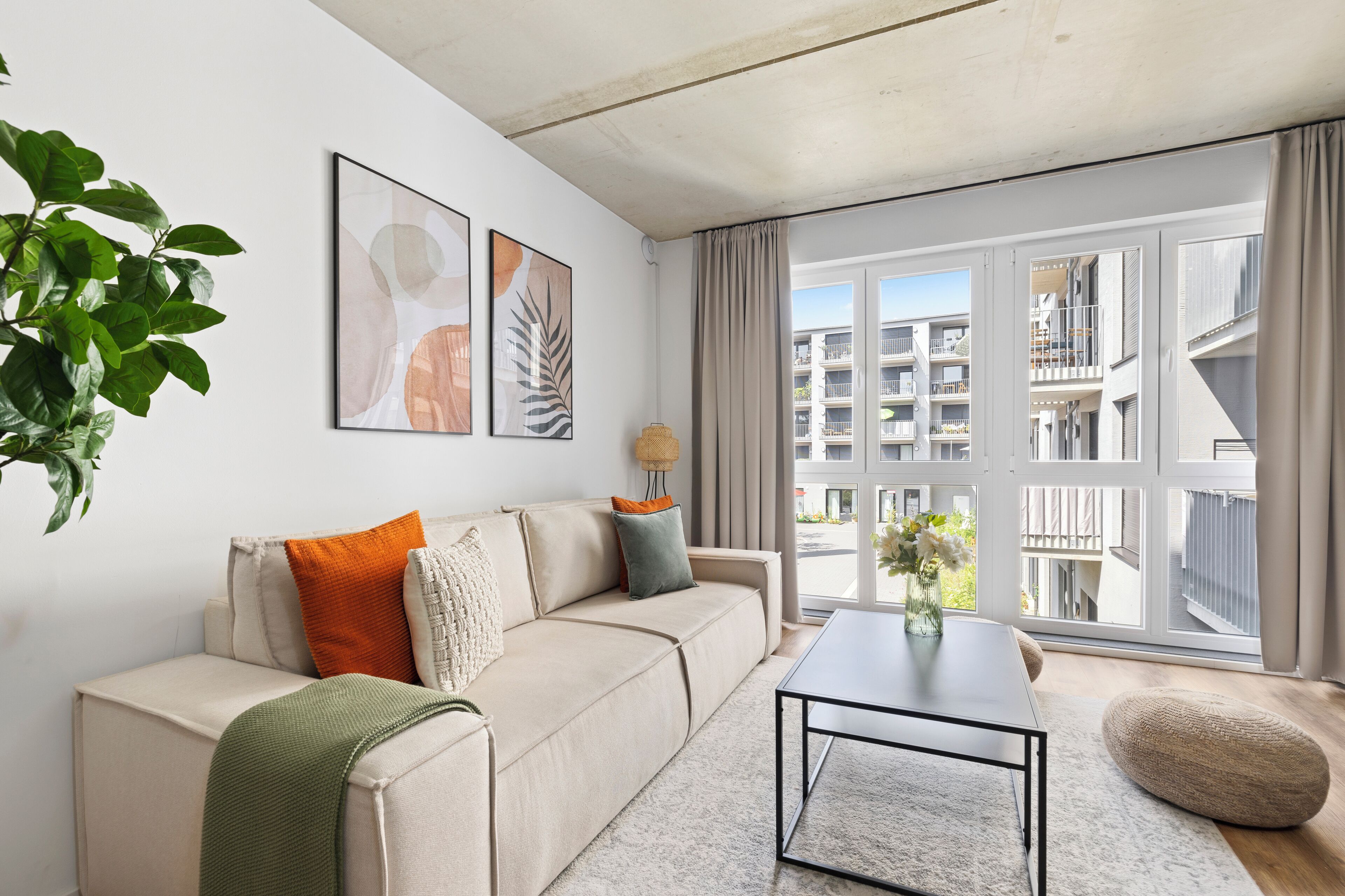 A modern living room with a sofa, coffee table, and large windows offering a view of the cityscape.