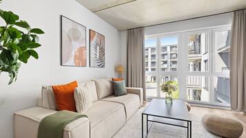 A modern living room with a sofa, coffee table, and large windows offering a view of the cityscape.