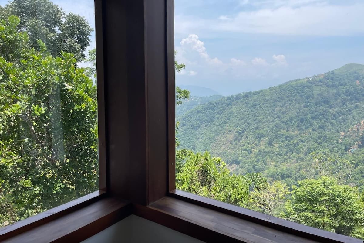 A corner of a room with a window overlooking a lush green landscape with hills.