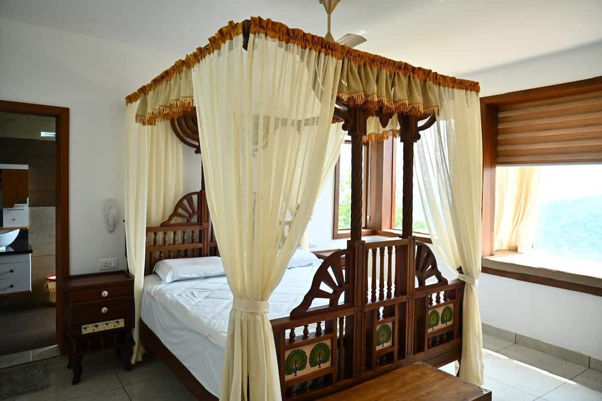 A four-poster bed with a canopy, wooden headboard with tree motifs, a bedside table, and a window with blinds.