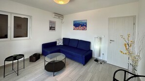 Una sala de estar moderna con un sofá azul, una mesa de centro de vidrio, una mesita auxiliar de mimbre y un aire acondicionado instalado en la pared.