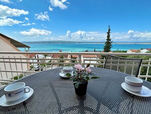 A balcony with a table set for two, overlooking a coastal view with a clear sky. - Apartman Adriatic Dream 1 (Crikvenica)