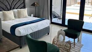 Ein modernes Hotelzimmer mit einem großen Bett, einem grünen Sessel, einem Beistelltisch und Blick auf den Pool.