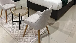 Ein modernes Schlafzimmer mit einem großen Bett, zwei Sesseln, einem kleinen runden Tisch und Blick durch eine Glastür.
