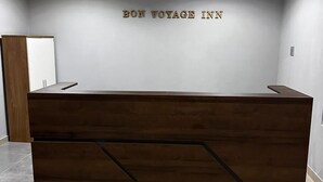 Ein Empfangsschalter mit modernem Design, mit dunkler Holzoptik und einem geometrischen Muster im unteren Bereich. An der dahinterliegenden Wand befindet sich der Schriftzug „BON VOYAGE INN“ in Goldfarbe.