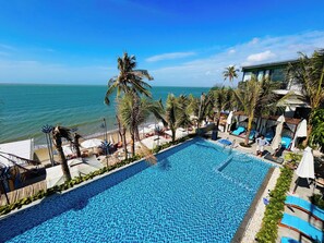 Área da piscina com vista para o oceano, cercada por palmeiras e espreguiçadeiras.