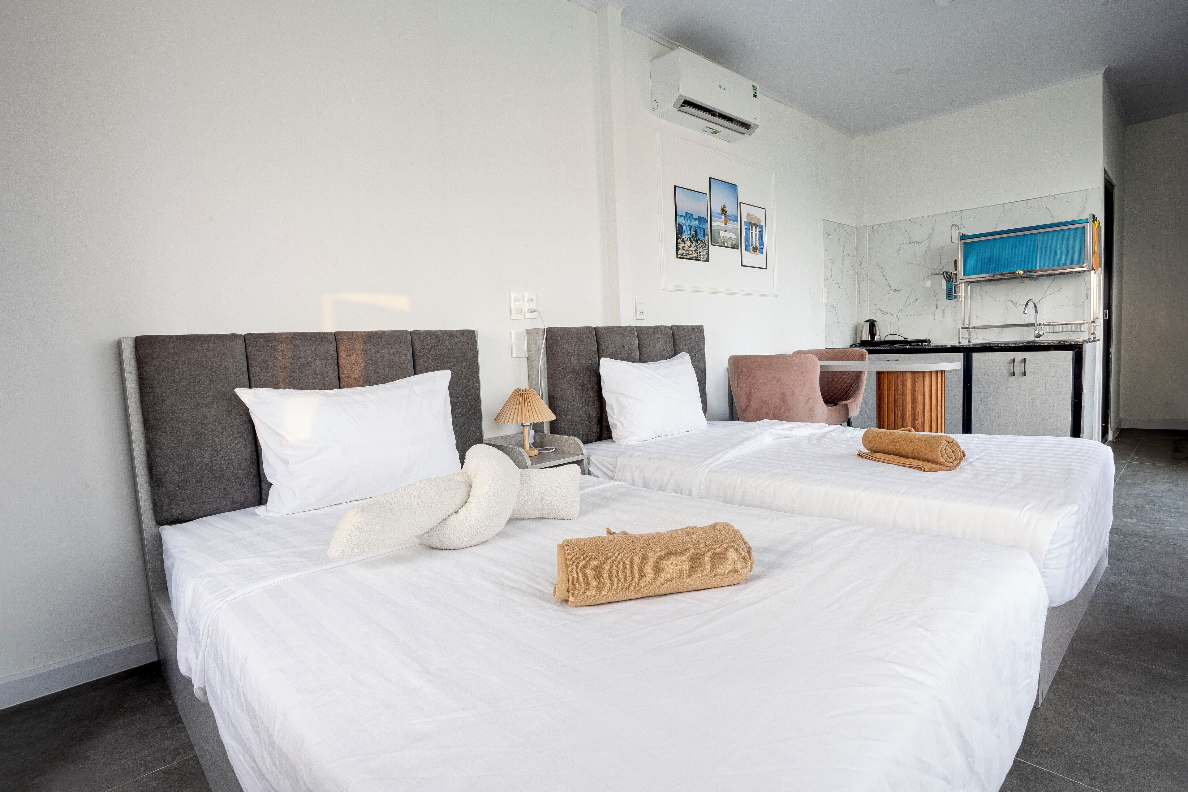 A hotel room with two beds, a small kitchenette, and a bathroom.
