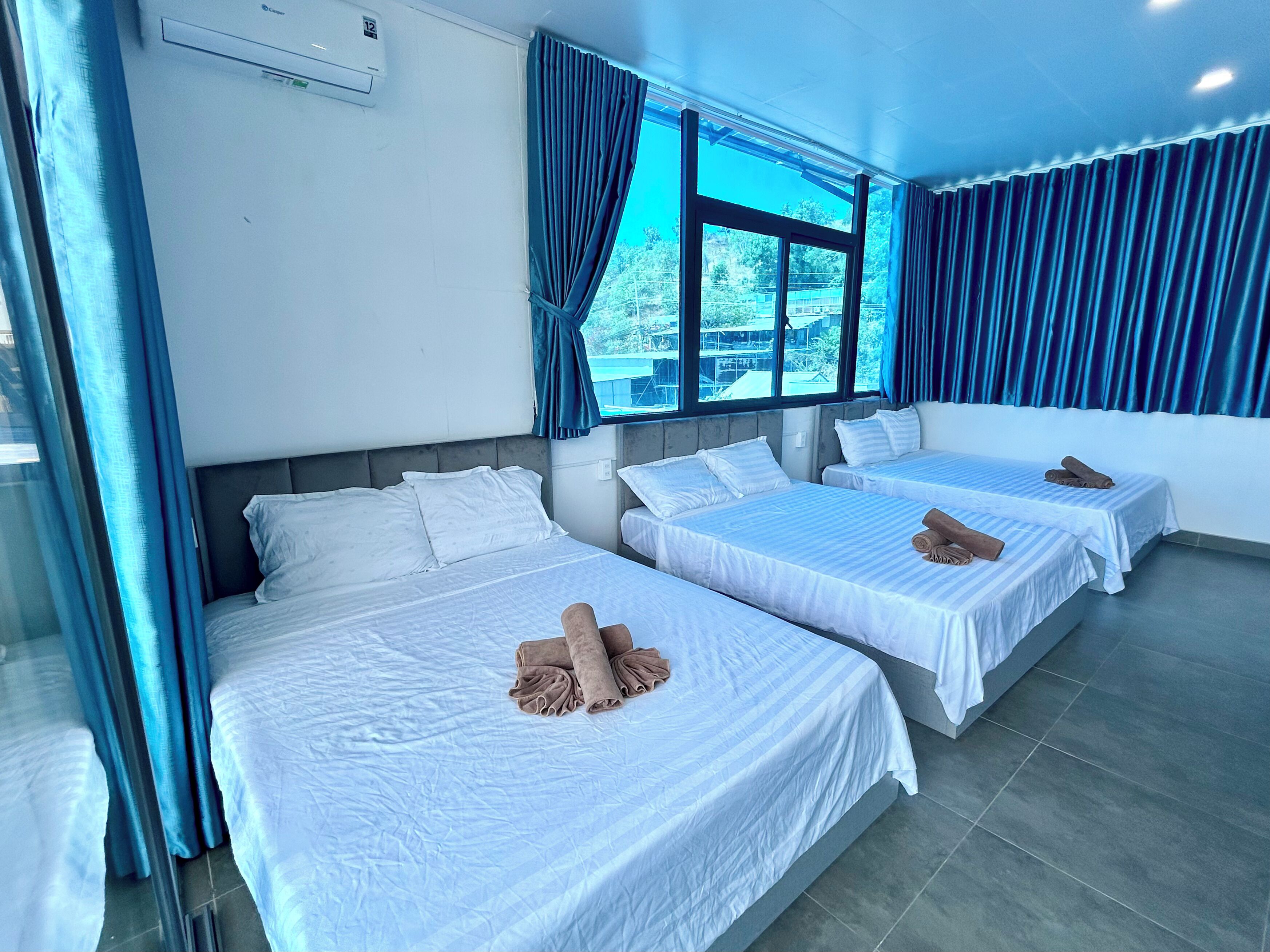 A hotel room with two beds, a large window with curtains, and a ceiling fan.